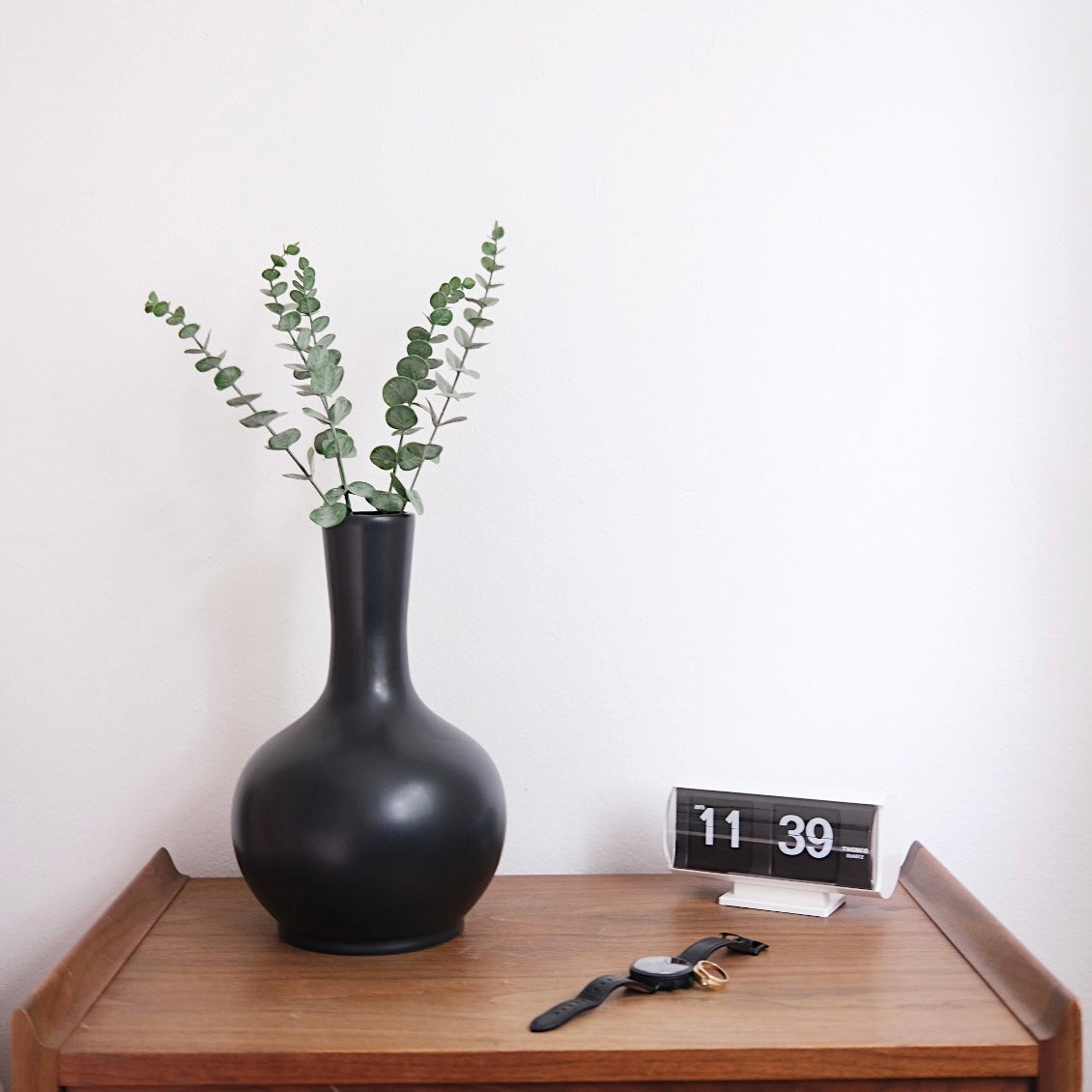 Black urn sitting on a nightstand next to an alarm clock