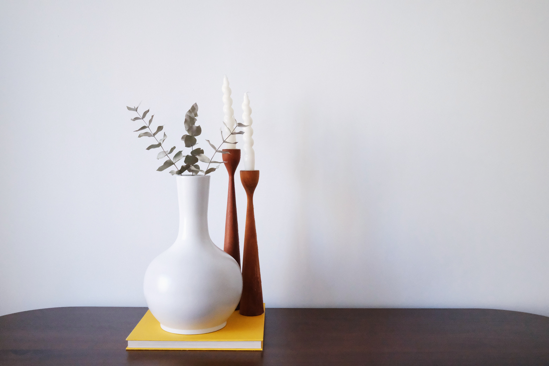 White urn vase sitting on a yellow coffee table book with candle sticks